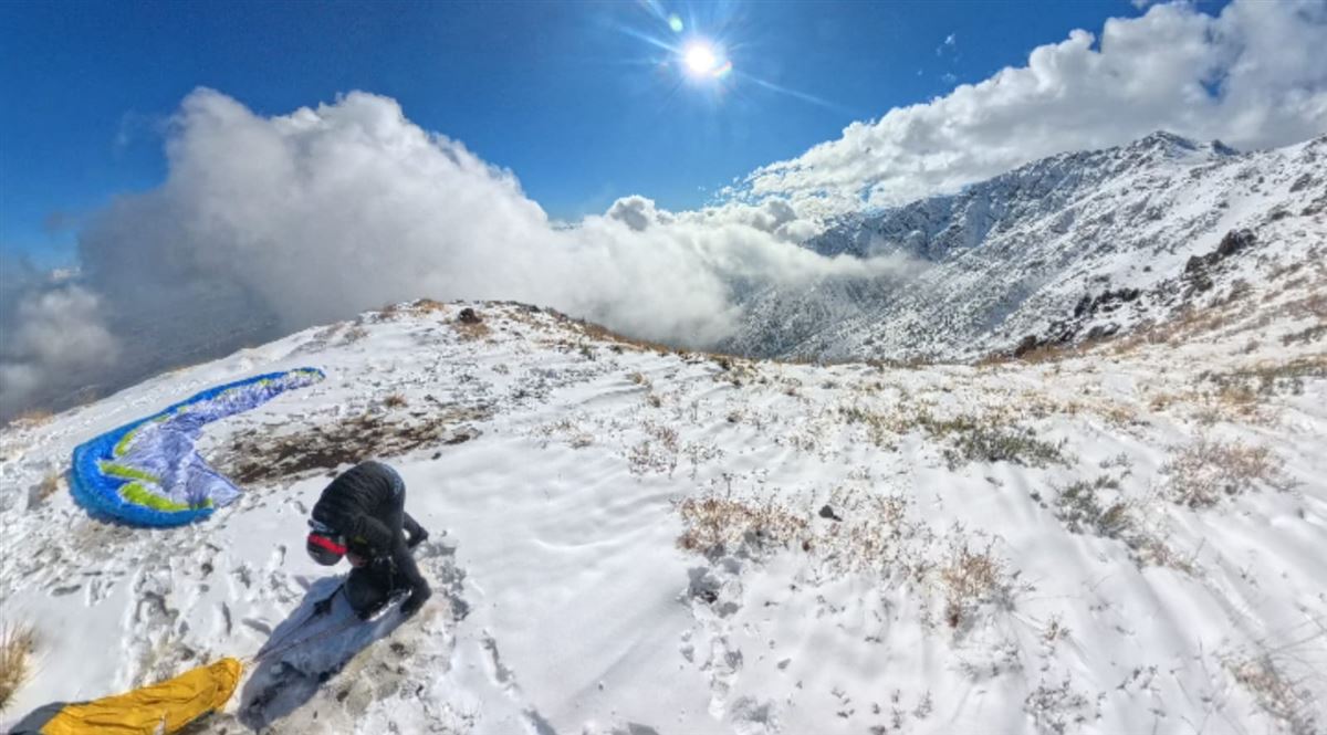 Piloto preparando el parapente en la cumbre nevada de un cerro durante la experiencia Tándem Hike&Fly